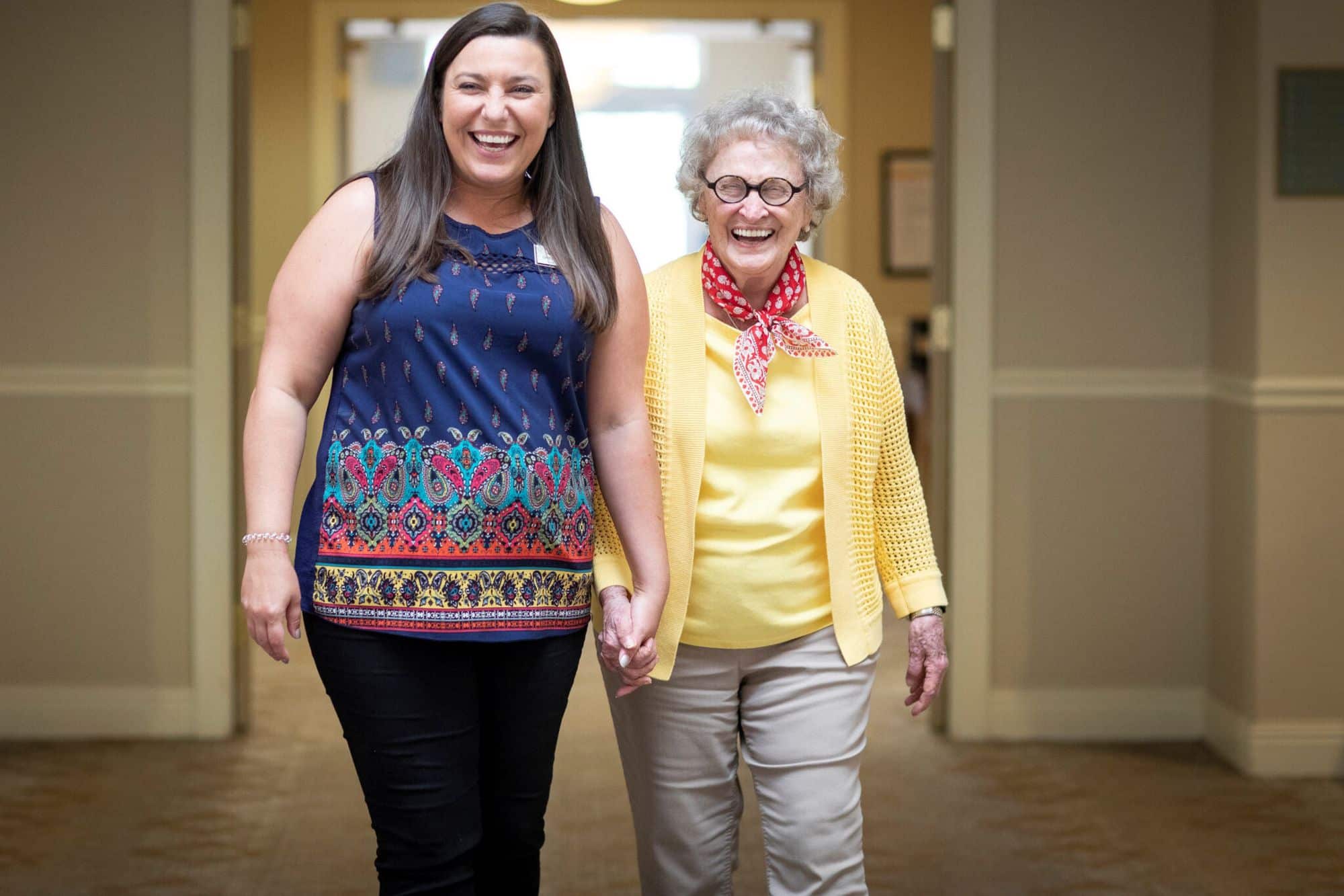 two people holding hands walking down a hallway of a senior independent living at celebration village forsyth.